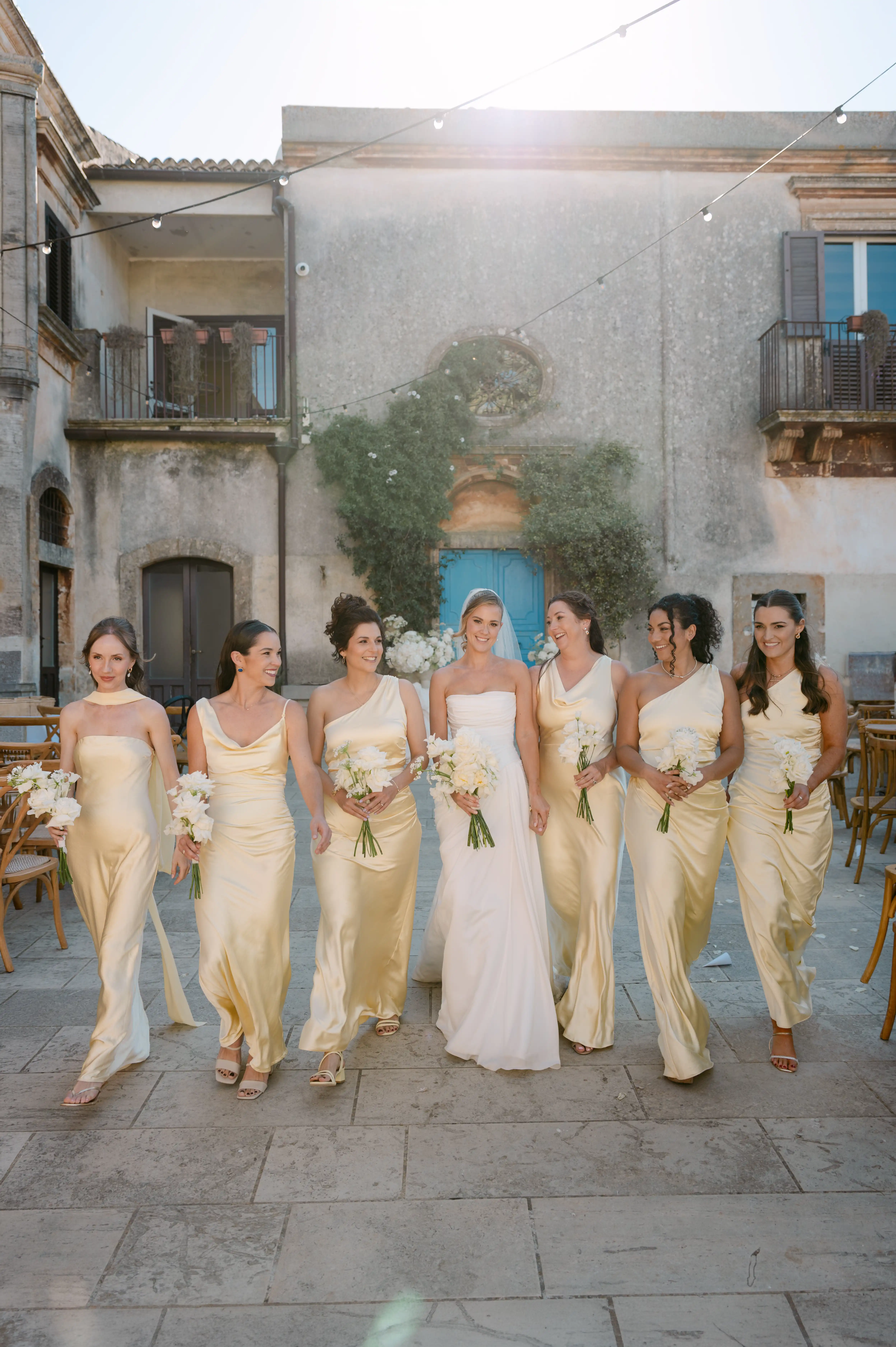 Bride walking with bridesmaids in champagne satin dresses at a luxury Sicilian wedding venue.